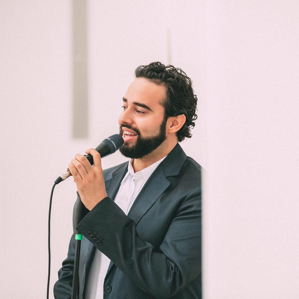 Mario Kempter der einfühlsame Tenor singt im dunkelblauen Anzug vor einem leicht rosa gefärbten Hintergrund. Seine Gesichtszüge sind sanft, freundlich und glücklich